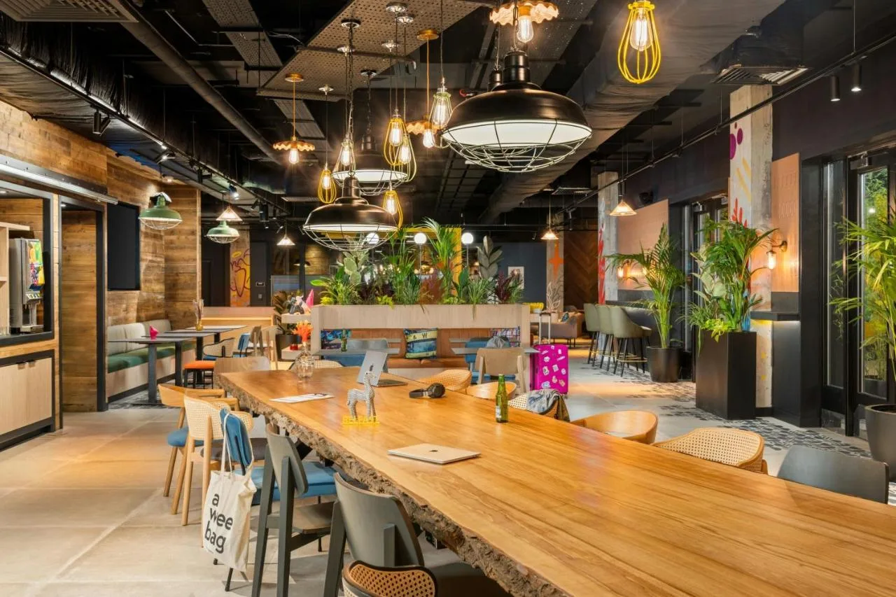 a restaurant with a large wooden table and chairs at Moxy Belfast City in Belfast